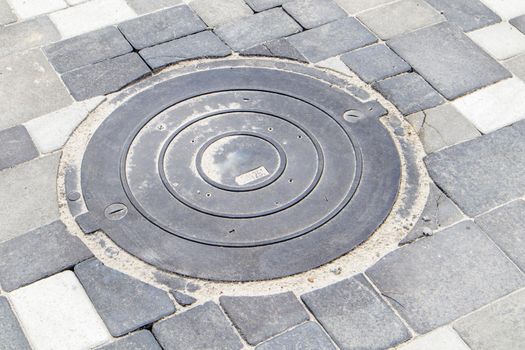 New plastic manhole cover on the sidewalk lined with gray paving slabs. The concept of sewerage, underground communications. Installation of a new sewer hatch. Construction industry