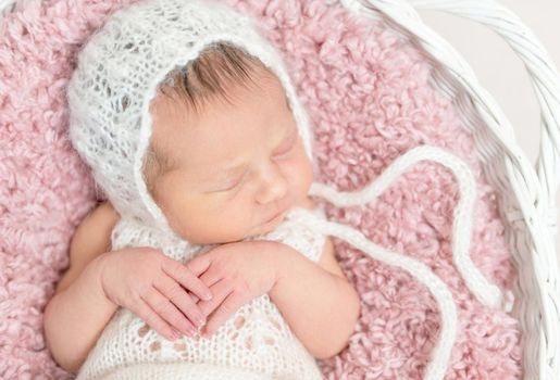 Adorable kid napping on big pink pillow wearing a hat and cute suit, in basket close-up