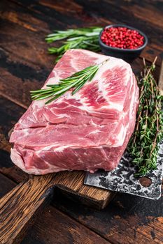 Pork neck raw meat for fresh Chop steaks on wooden cutting board with butcher cleaver. Dark wooden background. Top view.