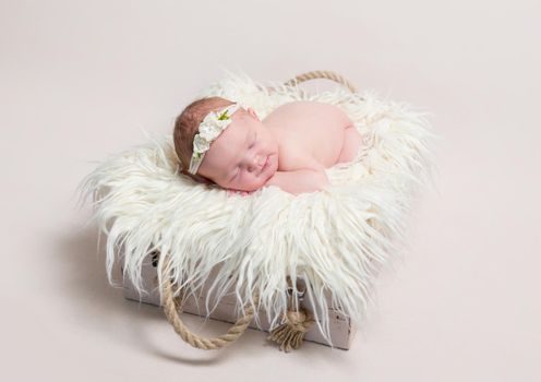 Sweet baby in hairband napping on her belly on adorable furry blanket in a basket