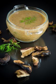 hot homemade vegetable vegetarian soup with dried mushrooms in a glass bowl on black background