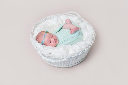 Adorable swaddled baby with legs moving, lying in kids basket, wearing headband