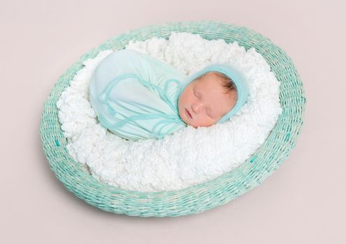 Adorable baby wrapped in blue blanket sleeping on white and blue bedding, in basket, topview