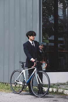 Portrait asian businessman pushing his bicycle in the morning with mobile phone.