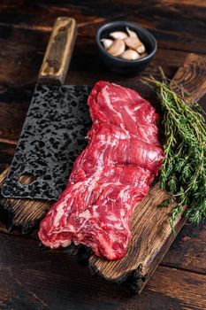 Raw machete skirt beef steak on butcher board with cleaver. Dark wooden background. Top view.