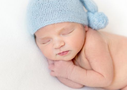 Close-up portrait of newborn little baby in blue bonnet smiling while sleeping