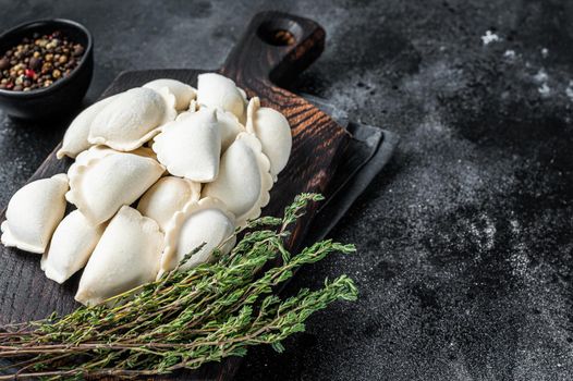 Frozen raw dumplings pierogi with potato on a wooden board. Black background. Top View. Copy space.