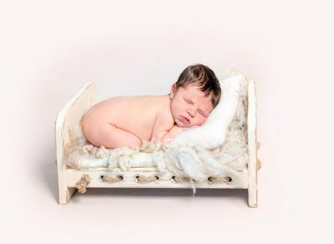 Adorable newborn baby sleeping on his stomach on wooden crib covered with furry rug