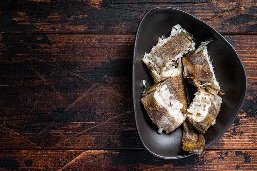 Roasted hake white fish in a plate. Dark wooden background. Top view. Copy space.