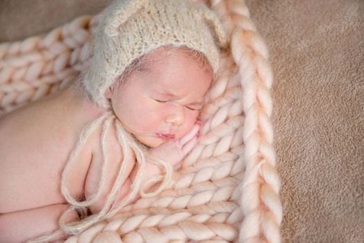 Sweetie newborn baby in beige bonnet sleeps on his tummy on knitted rug.