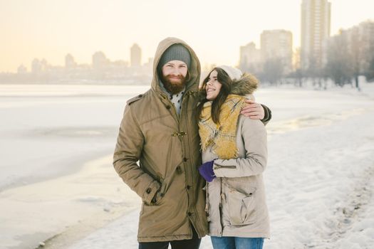 Theme love and date on nature. A young Caucasian heterosexual couple guy and girl walk in the winter along a frozen lake in winter. Bearded Man Hugging Woman. Valentine's day holiday.