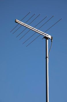 A metal television antenna on a a house roof against a blue sky background