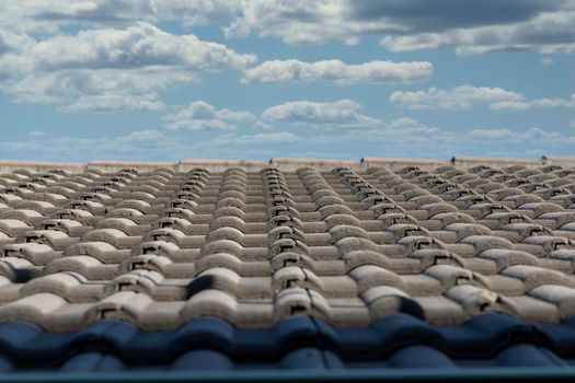 Grey terracotta roof tiles in a line on a roof in front of a bright blue cloudy sky background