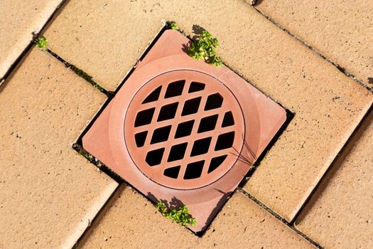 A stormwater drain cover inserted in brown paving stones near a swimming pool