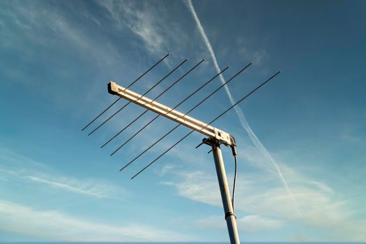 A metal television antenna on a a house roof against a blue sky background