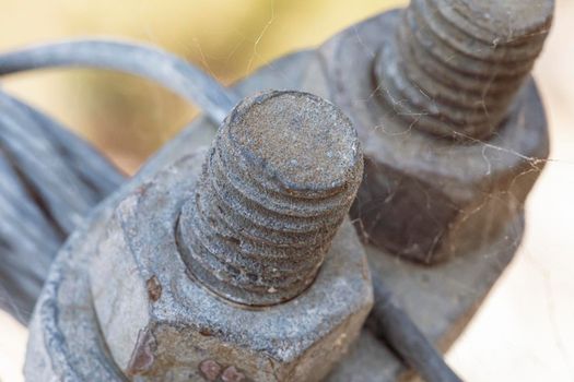 Photograph of the thread of a rusty galvanised bolt and nut securing a steel cable in a spiderweb