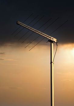 A metal television antenna on a a house roof against an orange sunset sky background
