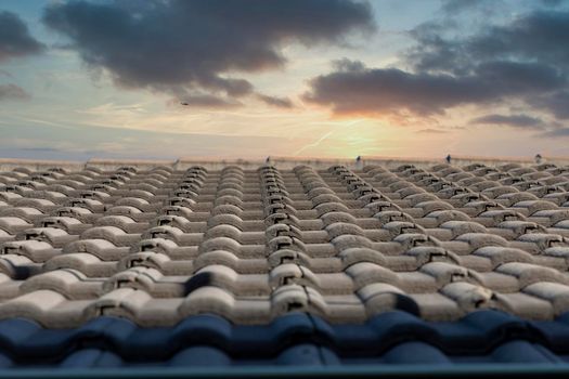 Grey terracotta roof tiles in a line on a roof in front of a sunset sky background