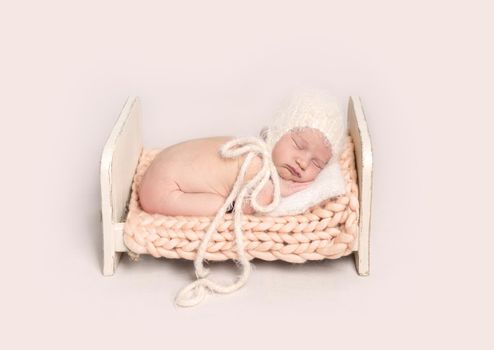 Little infant baby in white bonnet sleeping peacefully on tummy on small wooden crib