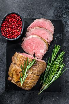 Roast beef fillet Tenderloin meat on a marble board. Black background. Top view.