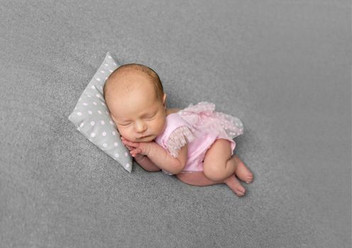 Lovely newborn girl in pink dress sleeping with pillow under her little head. Little princess with flowery hair band sleeping on her side