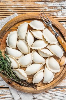 Homemade raw frozen dumplings, vareniki, pierogi stuffed with potato on a wooden board. White wooden background. Top View.