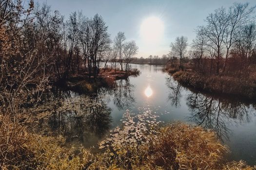 Vivid autumn sunset. Autumn landscape of sunset over river with shining grass on shore. Scenic nature at bright evening with colorful sky.