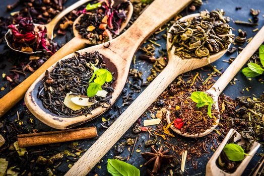 Virious kinds of tea in wooden spoons on black table