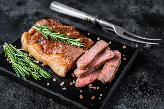 Cut roasted new york strip beef meat steak or striploin on a marble board. Black background. Top view.