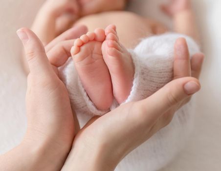 Mom holding little baby's legs wearing in white knitted pants