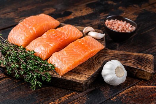 Fresh Raw salmon fish fillet steaks on wooden board with thyme. Dark wooden background. Top view.