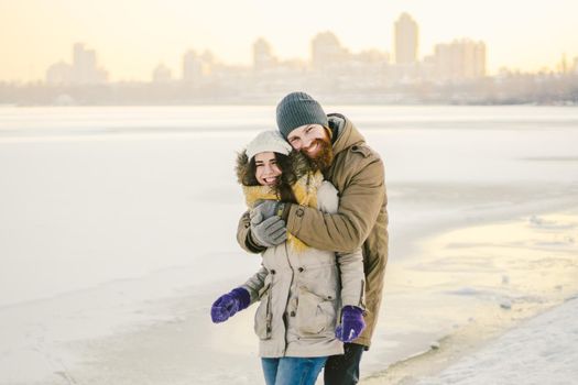 Young couple cheerfully flounders in snow. Between comic fight. Happy young couple hugs in winter snowy woods. Romantic lifestyle men and women in love. St. Valentine Day date Christmas hugging happy.