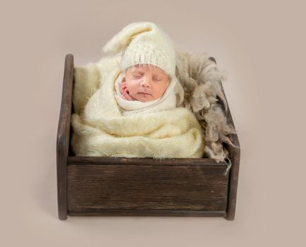 Cute little baby in hat sweetly sleeping in small bed covered in blanket