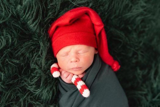 Cute baby in red santa hat sleeping with knitted candy stick