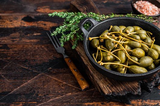 Marinated canned capers in a pan. Dark wooden background. Top view. Copy space.