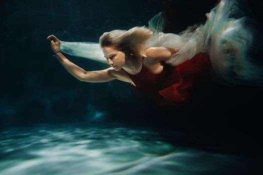 A girl in a red dress is swimming under the water.Journey under the water of a single woman.The concept of underwater tourism.