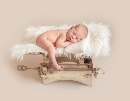 Cute newborn baby on a retro weight scale on beige background