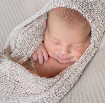 wrapped cute newborn baby sleeping with smile, close up