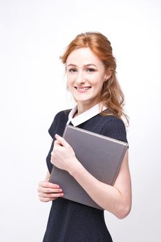 Beautiful girl with red hair and gray book in hands dressed in black dress on white isolated background.