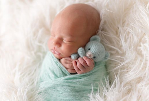 Newborn boy lying wrapped in a blanket with favorite knitted blue teddy bear