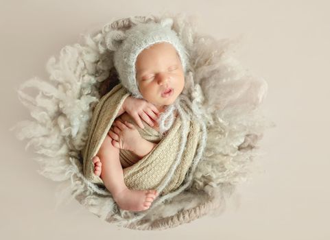 Adorable newborn child sleeping on fluffy wool blanket in little knitted hat