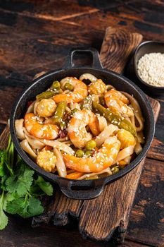 Asian Udon stir-fry noodles with shrimps prawns in a pan. Dark wooden background. Top view.
