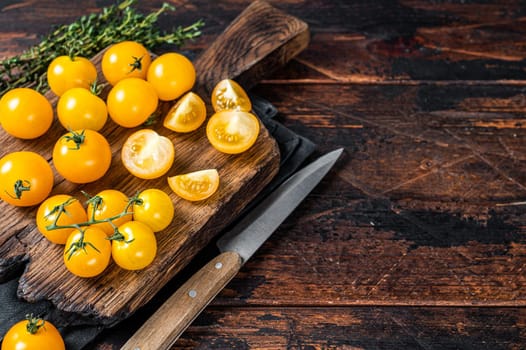 Yellow cherry tomato sliced on a wooden cutting board. Dark wooden background. Top view. Copy space.