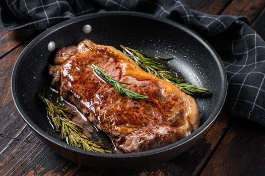 Grilled new york strip beef meat steak in a pan with herbs. Dark wooden background. Top view.