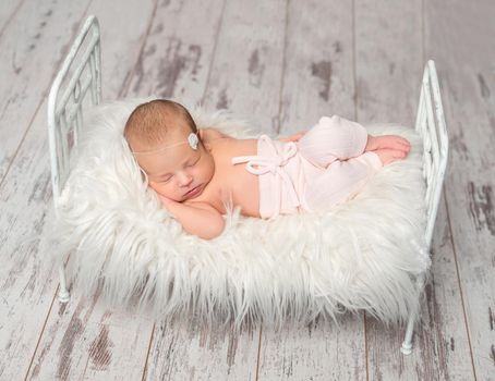 newborn sleeping baby in panties holding toy on cute little bed with white fluffy blanket