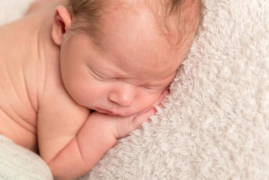 Infant pressing his hands to his cheek, sleeping on a white carpet, closeup