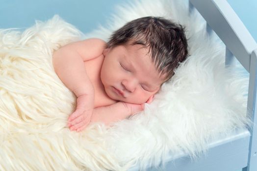 Tranquil infant sleeping on his side, covering himself with a white blanket, closeup