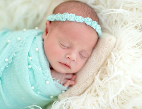 Sleeping adorable newborn baby child, in blue colored blanket and with floral headband