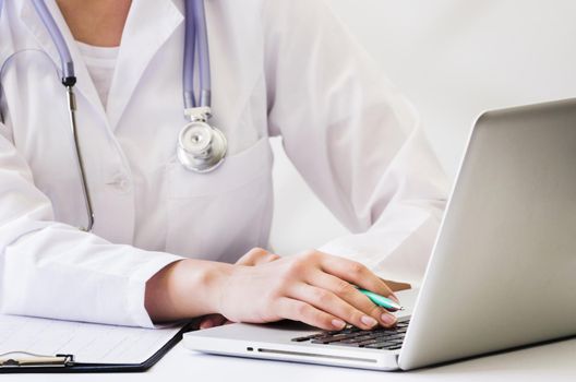 female doctor with stethoscope around her neck using laptop desk