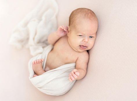 Cute awake newborn touching his ear with hand